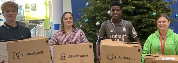 A group of students stood in front of a Christmas tree holding boxes of books